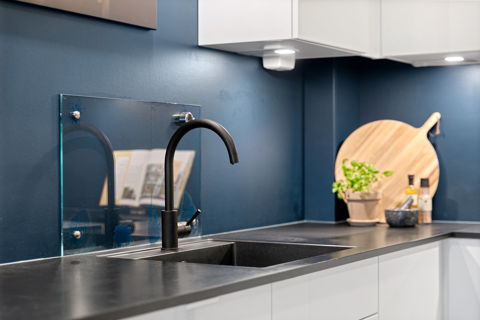 Hvite glatte fronter og en mørk benkeplate mot veggfargen gir kjøkkenet et delikat preg Galleribilde