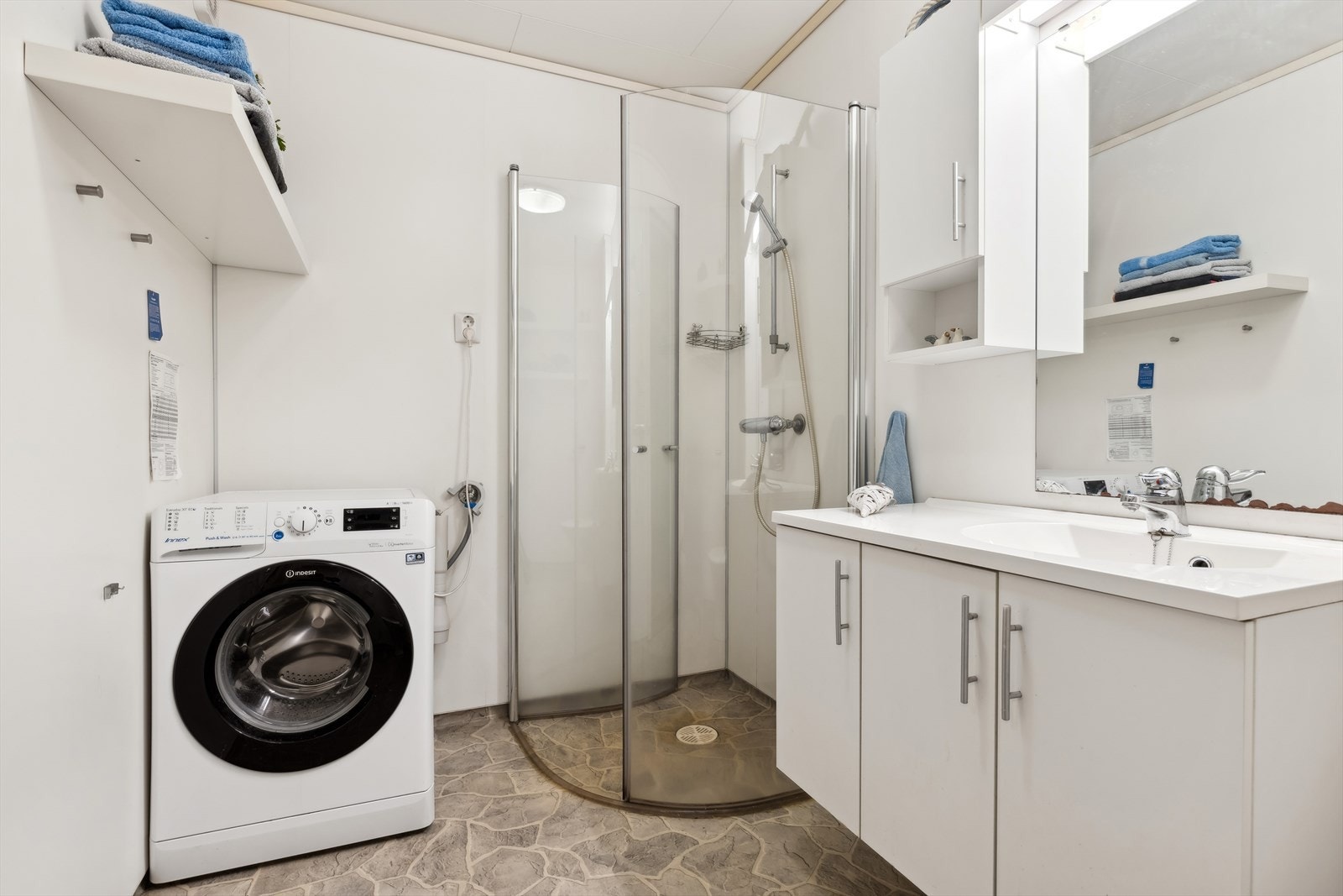 Badet har montert dusjhjørne, baderomsinnredning med servant og vanntilørsel/avløp til vaskemaskin i rommet. Galleribilde