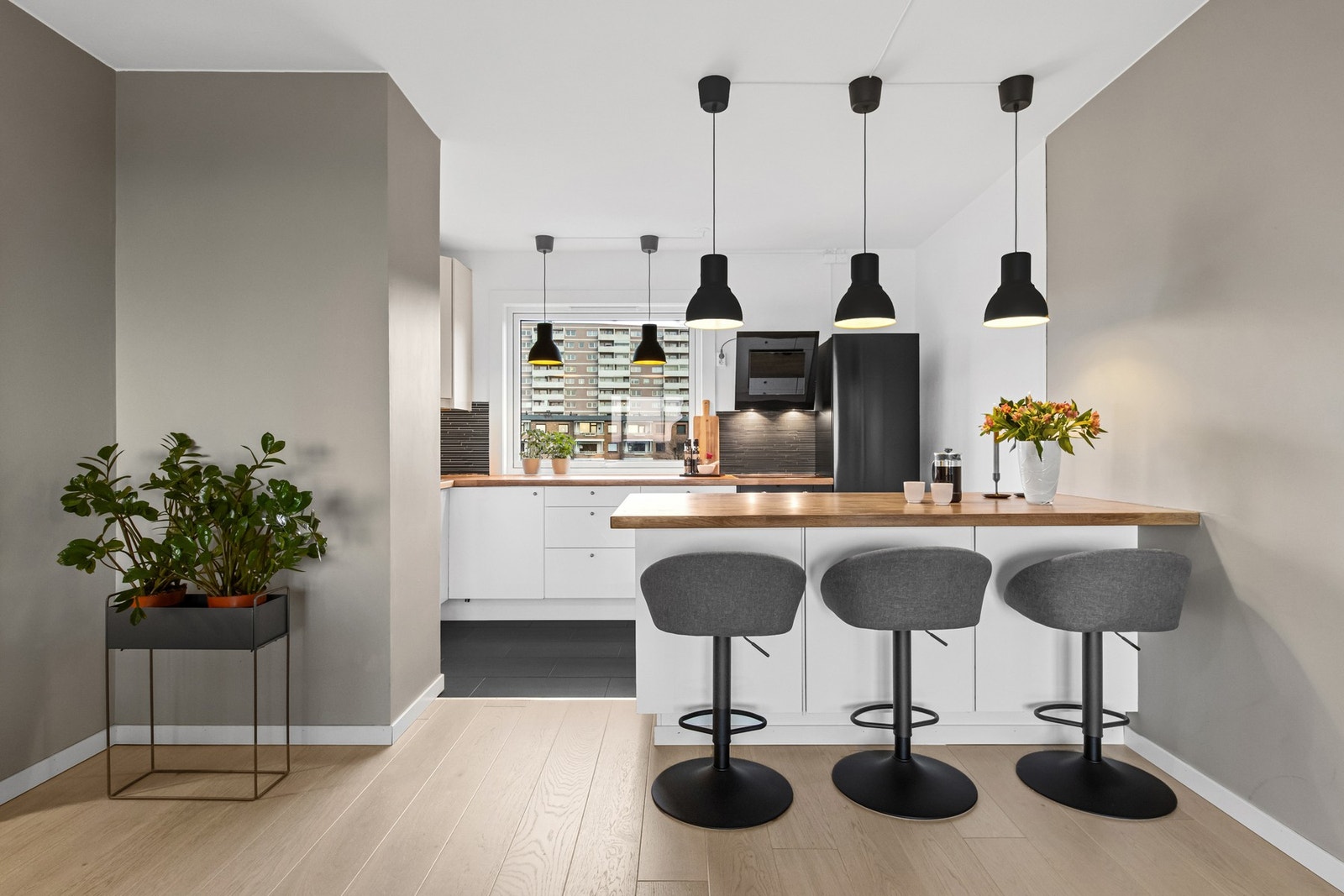 Kjøkkenet danner en egen sone, markert med mørke fliser på gulvet, hvitmalte vegger og en sosial barløsning i grensen mot stuen. Galleribilde