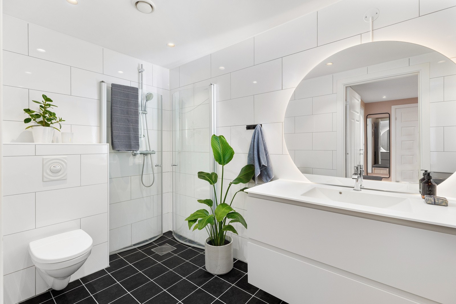 Stort og tidløst bad med mørke gulvfliser med varmekabler, hvite veggfliser og downlights i himling. Galleribilde