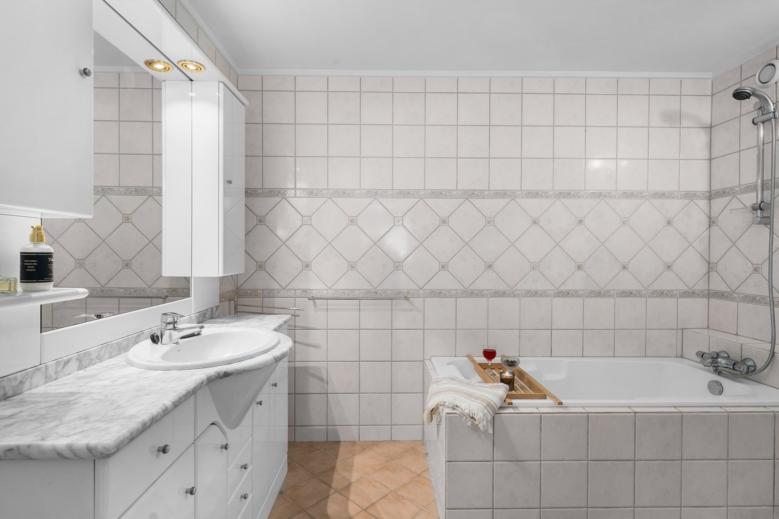 Romslig flislagt baderom med tidløs innredning og badekar Galleribilde