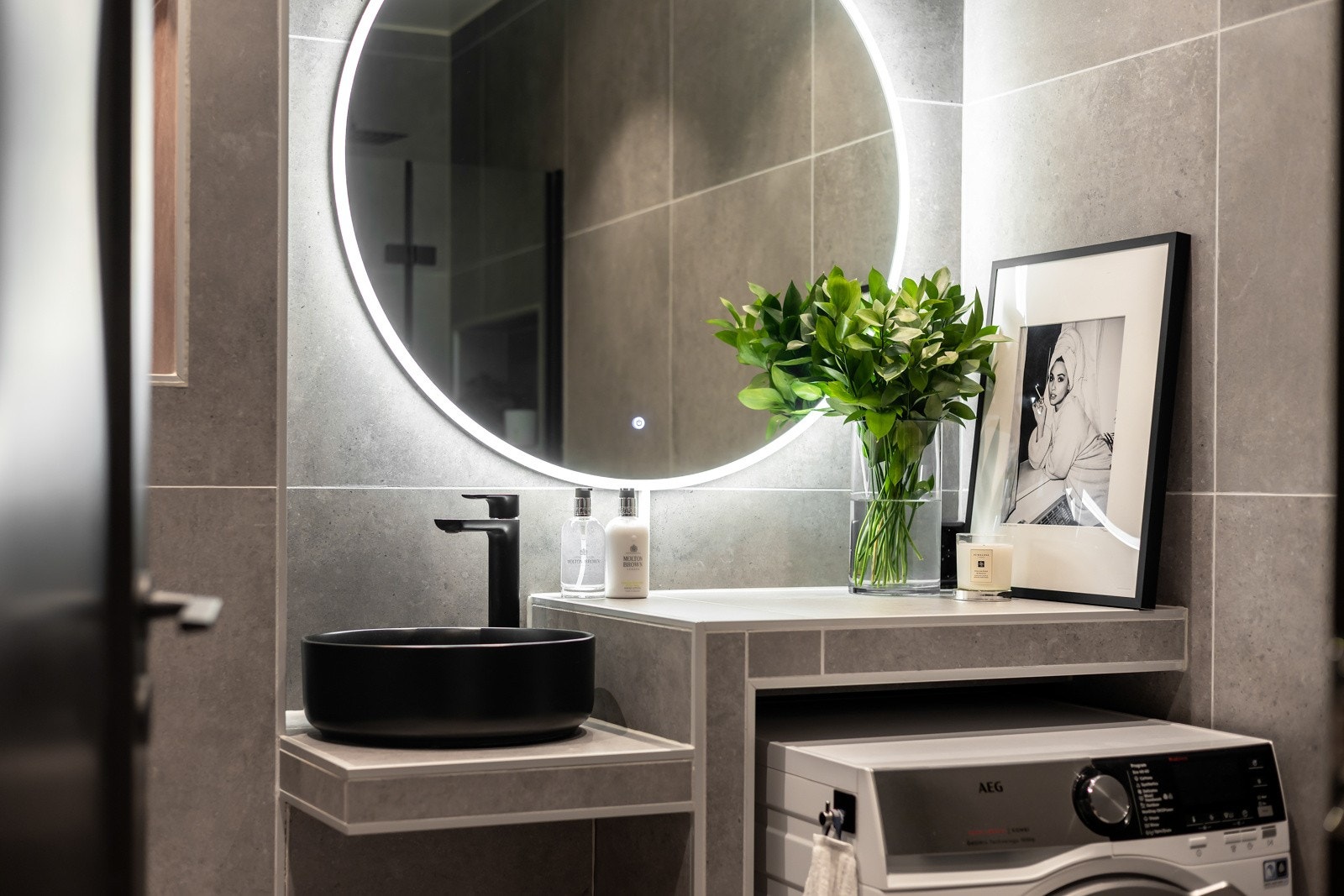 Badet er pent flislagt og innredet med et toalett, dusjnisje med glassdør og en servantinnredning med nisje for vaskemaskin. Galleribilde