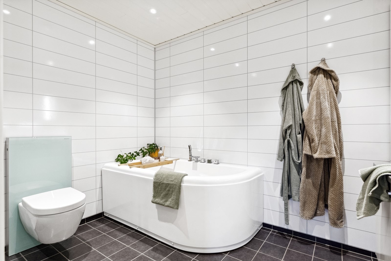 Stilen er klassisk med hvite flisplater på veggene og grå fliser på gulvet. Det er også downlights og gulvvarme. Galleribilde