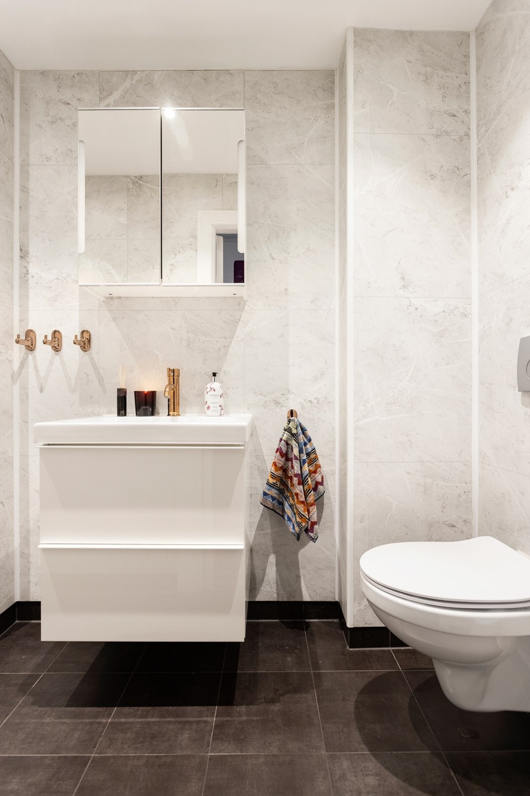 Baderom, med adkomst fra gang, pusset opp i 2020. Helservant med underskuffer. Speilskap over servant. Vegghengt toalett. Galleribilde