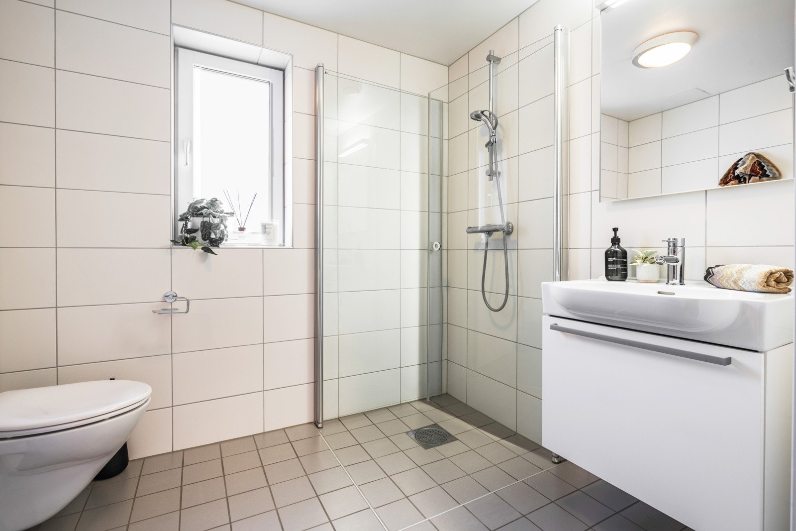 Badet er utstyrt med vegghengt toalett, et romslig dusjhjørne, servantskap med innredning og speil med belysning. Galleribilde