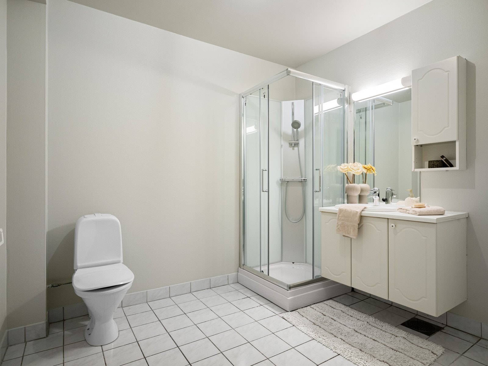 Baderom med fliser på gulv, toalett, nytt dusjkabinett og baderomsinnredning med skap for oppbevaring Galleribilde