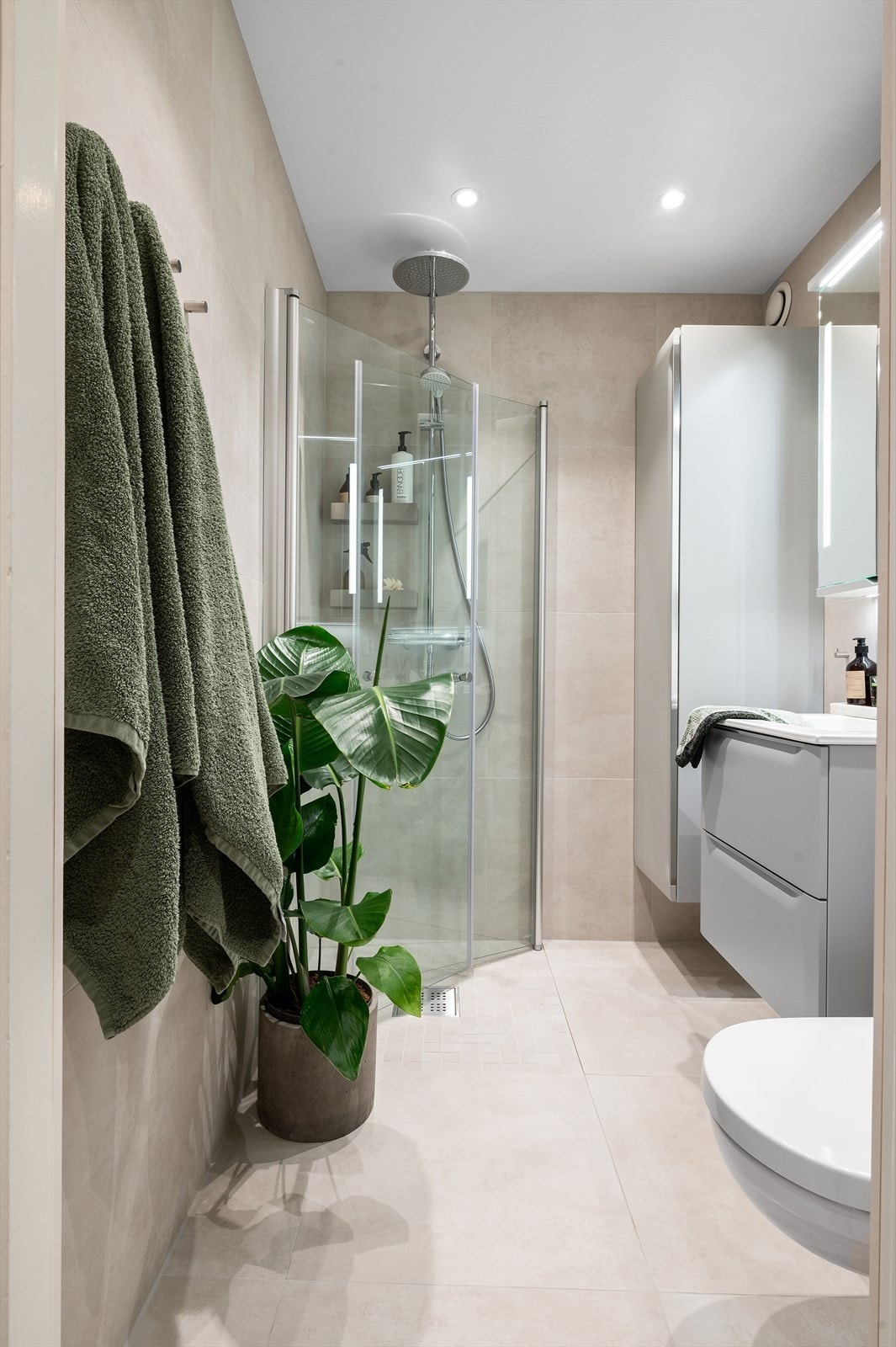 Delikat baderom fra 2022, med flislagte overflater og gulvvarme, samt malt himling med downlights. Galleribilde