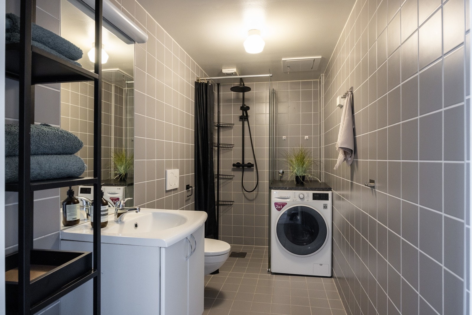 Stort, flislagt baderom som består av toalett, dusjhjørne, servant over innredning og speil. Galleribilde