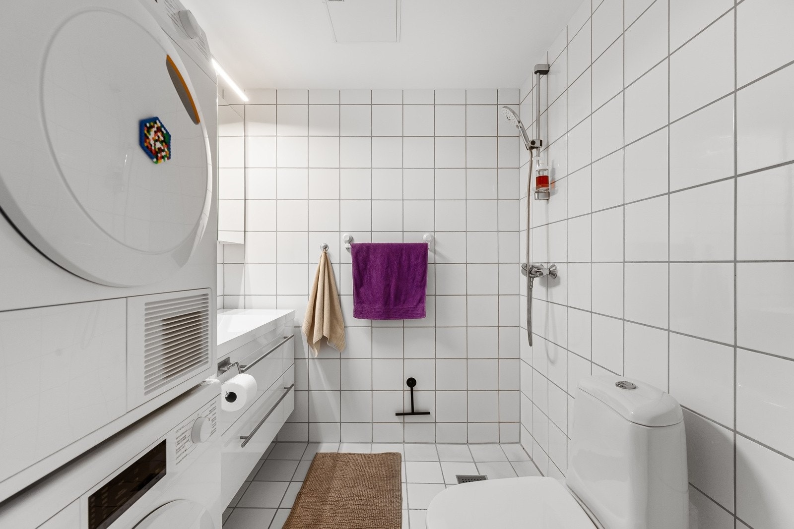 Fint, flislagt baderom som består av dusjhjørne, toalett, servant over innredning og speil. Galleribilde