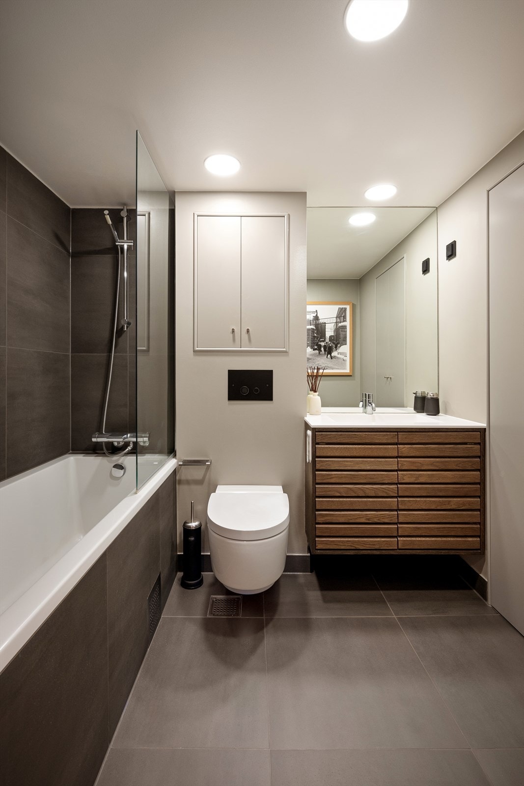 Delikat flislagt baderom med dusjtoalett og innredning fra danske Svane Kjøkken med corian-vask og Vola armatur Galleribilde