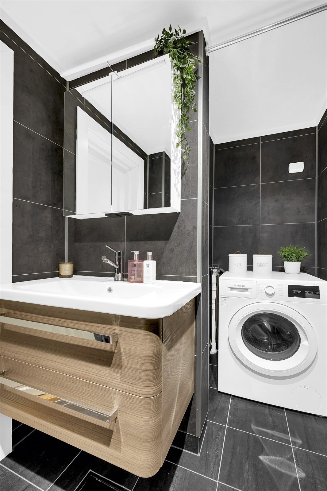 Badet er utstyrt med gulvmontert toalett, dusjhjørne med innfellbare glassdører og baderomsinnredning med skuffer, servant nedfelt i innredning og speilskap med belysning. Galleribilde