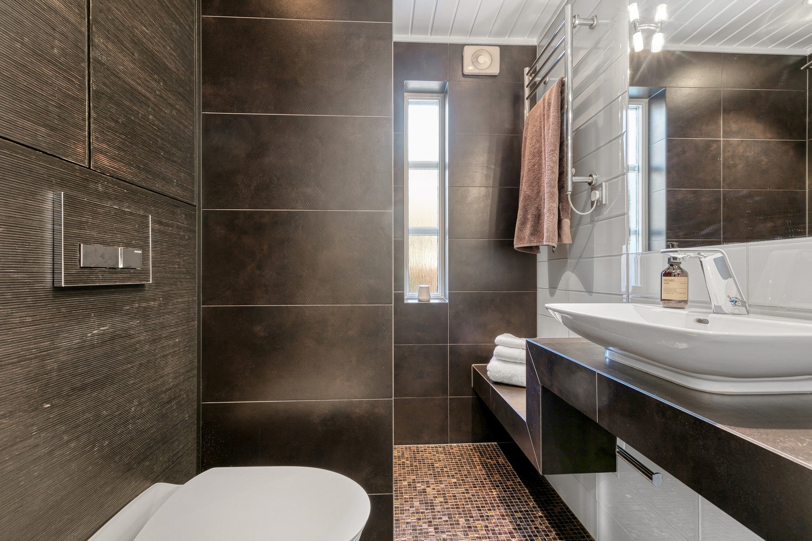 Bad ved entré (2012) med fliser, varmekabler og innredning med servant, håndkletørker, dusjnisje og toalett. Galleribilde