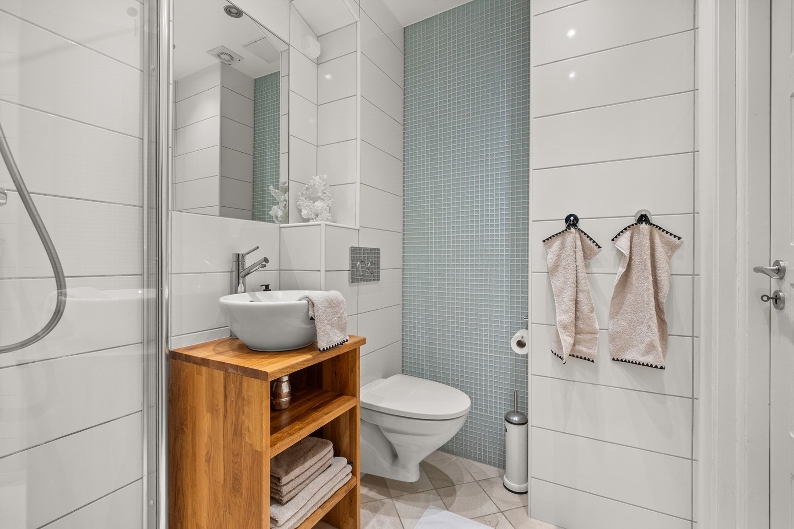 Badet har en tidløs stil med hvite veggfliser og sandfargede gulvfliser med gulvvarme. Galleribilde