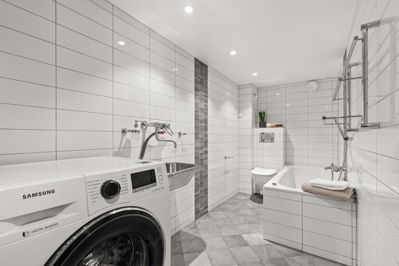 Det andre badet ligger i u. etasjen. Badet er innredet med tidløse hvite og grå fliser og har innmurt badekar, samt vegghengt wc. Galleribilde