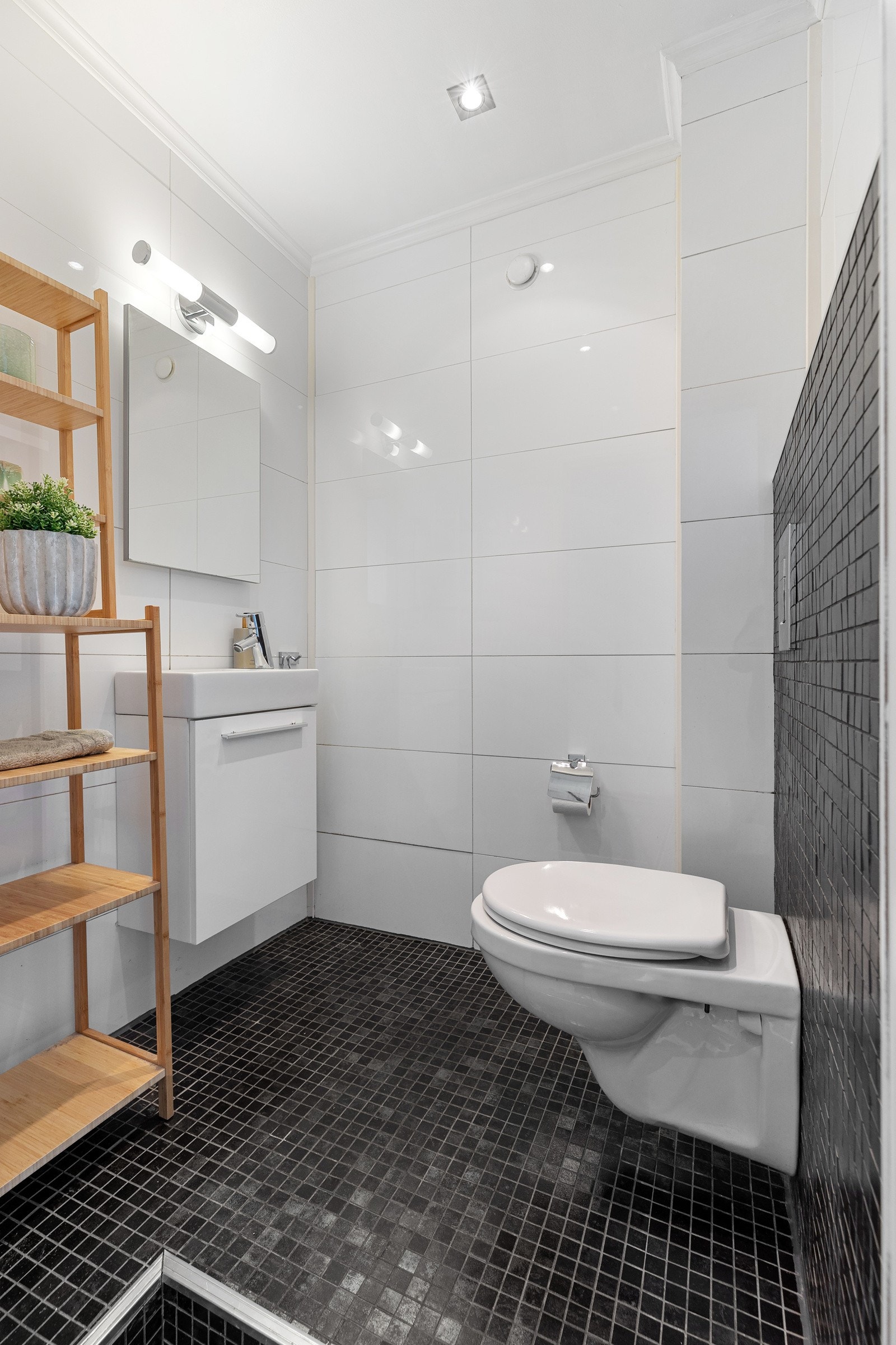 Separat toalettrom med mørke mosaikkfliser på gulvet og lyse vegg- og takflater Galleribilde