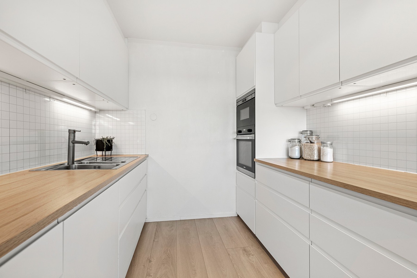 Tidløs kjøkkeninnredning med lyse flater og laminert benkeplate med nedfelt oppvaskkum med ett-greps armatur. Galleribilde