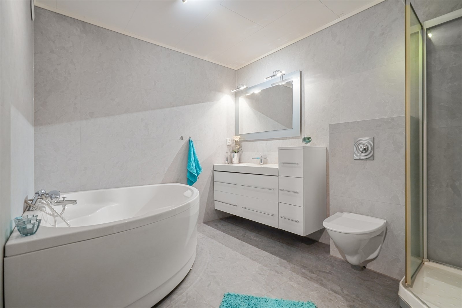 Badet er nylig renovert og fremstår som lyst og tiltalende. Badet er utstyrt med badekar, hvit innredning, dusjkabinett og vegghengt toalett Galleribilde