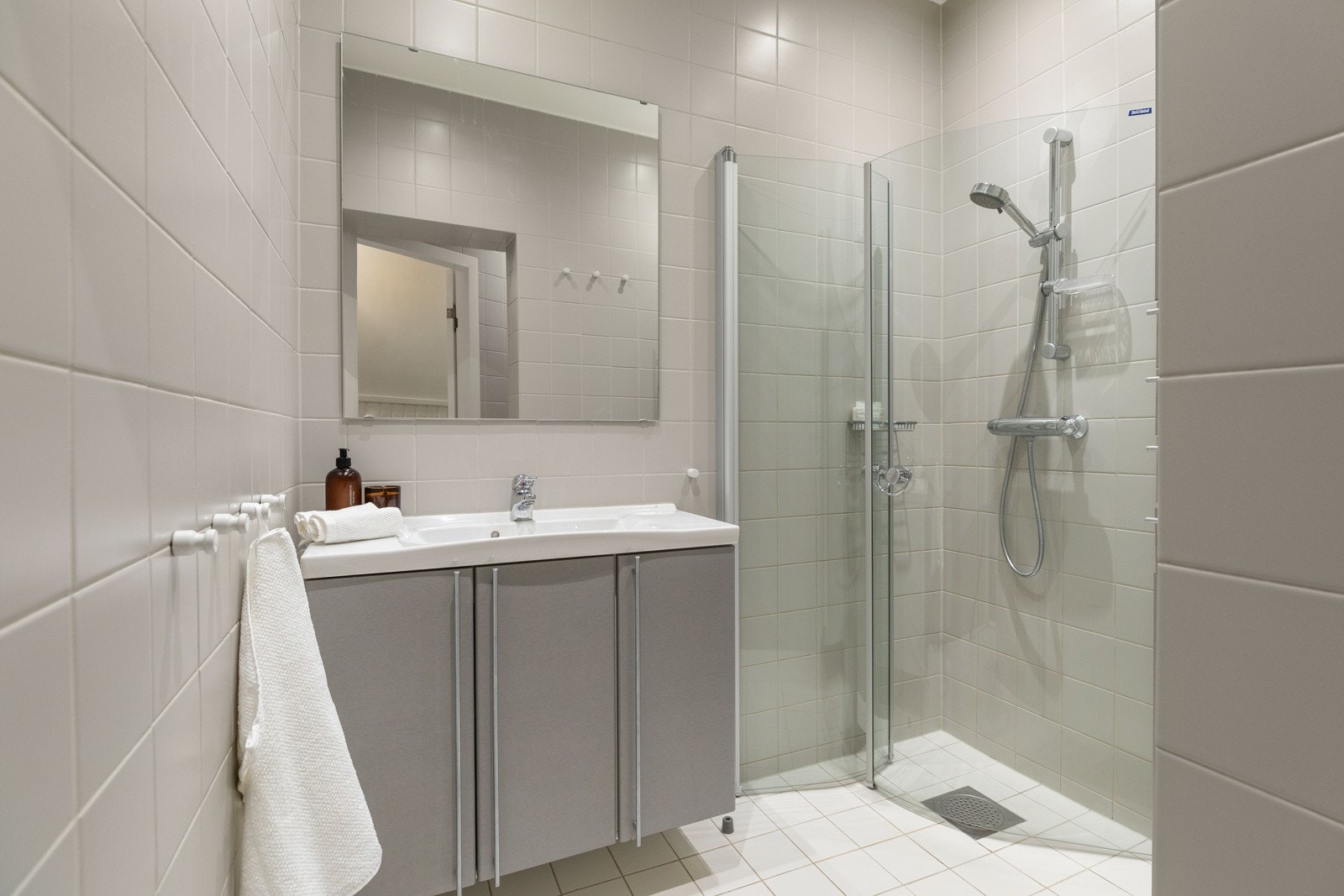 Badet innholder dusjhjørne med innfellbare dører, vegghengt wc i egen nisje, nedfelt servant i skapinnredning samt stort speil Galleribilde