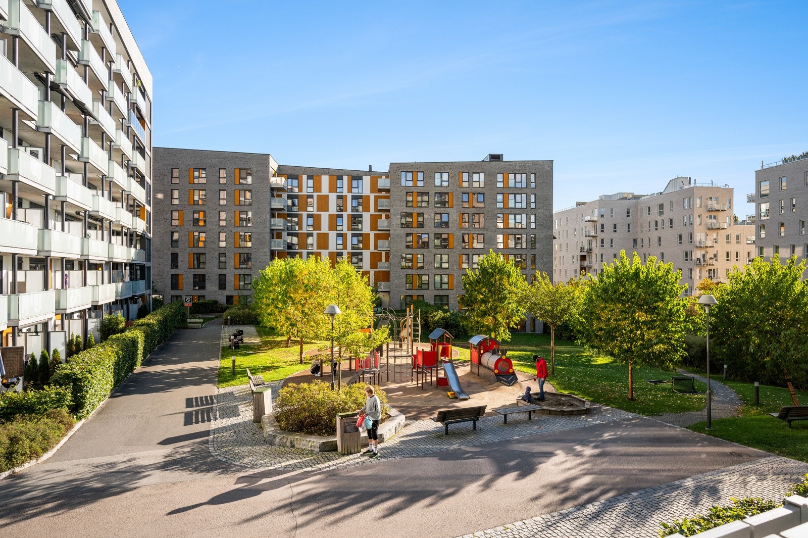 Pent opparbeidede fellesarealer med gressplen, trær, sittegrupper og lekestativ. Galleribilde