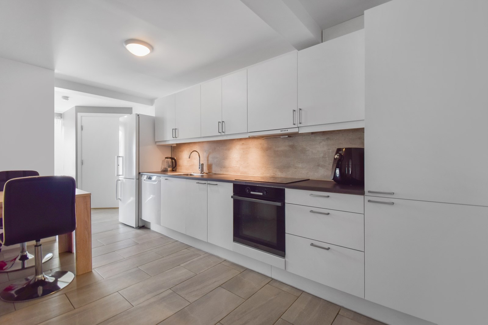 Ensidig Sigdal kjøkkeninnredning utstyrt med innfelt oppvaskmaskin m/ sensor, komfyr med nedfelt platetopp i benkeplate og frittstående kjøleskap. Galleribilde