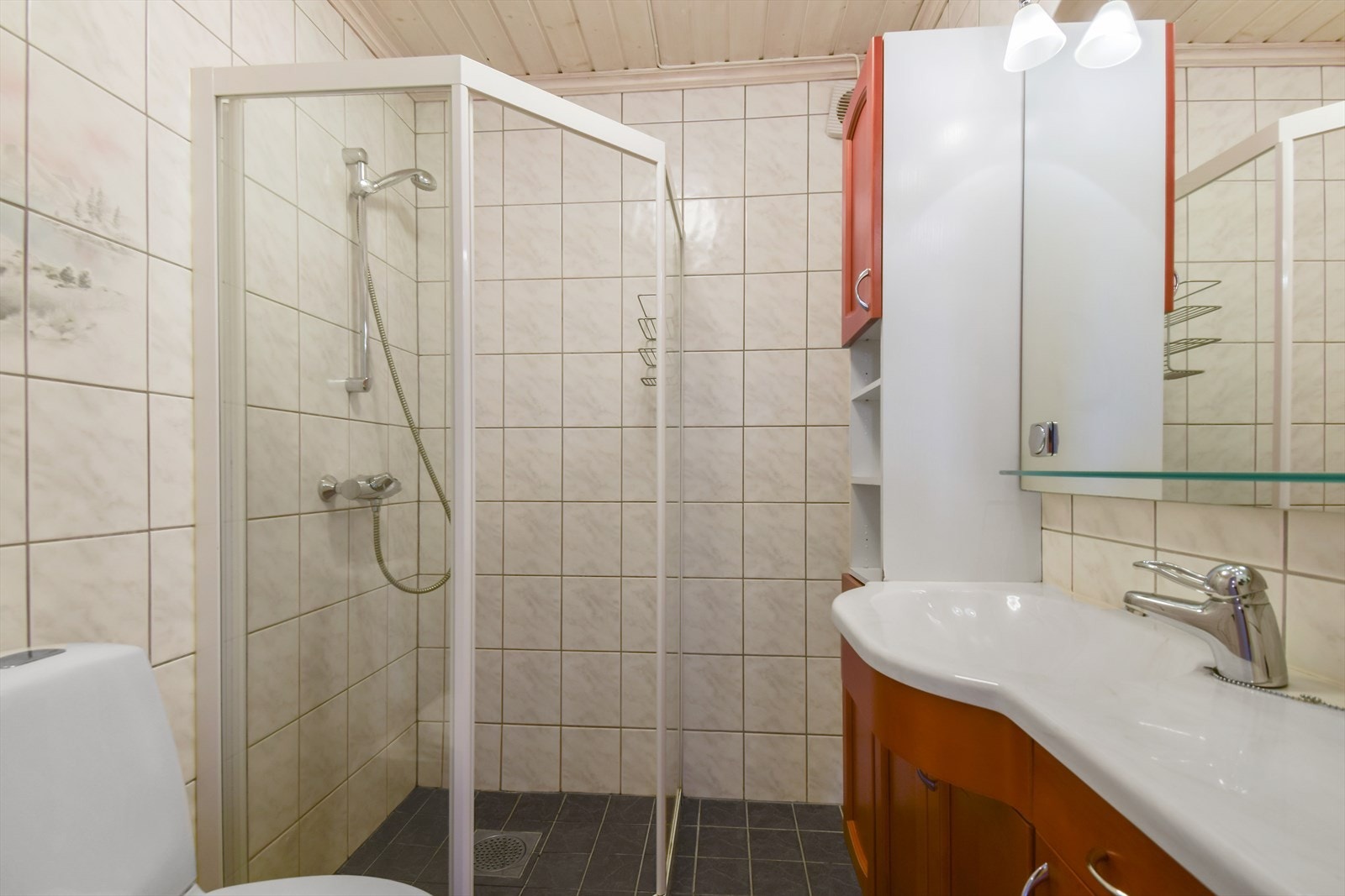 Helfliset bad utstyrt med dusjnisje, sluk i gulv, wc og vegghengt baderomsinnredning med servant. Galleribilde