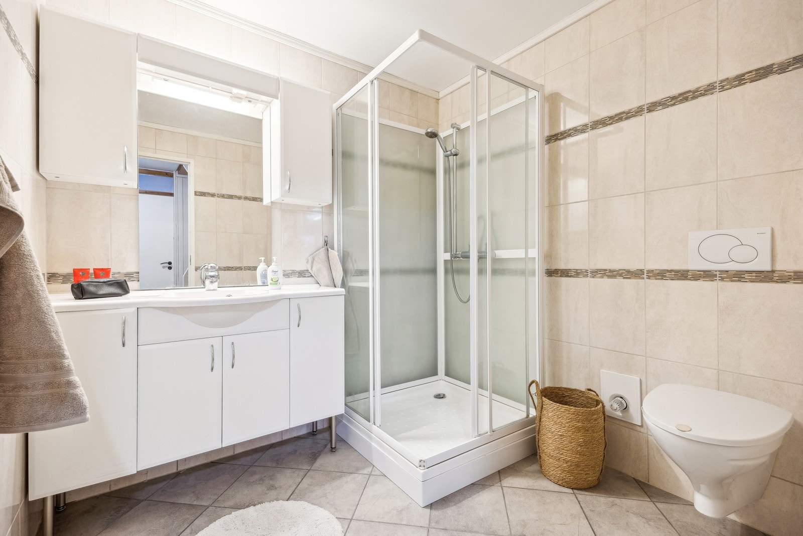 Det 5 kvm store badet er innredet med lyse fliser på vegger og gulv. Badet er innredet med et stort baderomsmøbel med mye oppbevaringsplass, dusjkabinett og vegghengt toalett. Galleribilde