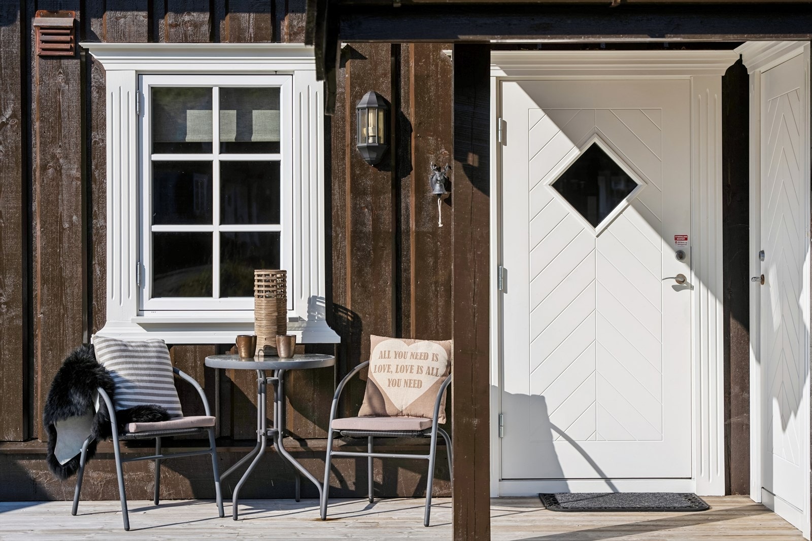 Inngangspartiet badet i morgensol, med en hyggelig plass perfekt for morgenkaffen. Overbygget gir ly for været, og det er direkte inngang til sportsboden for praktisk oppbevaring. Galleribilde