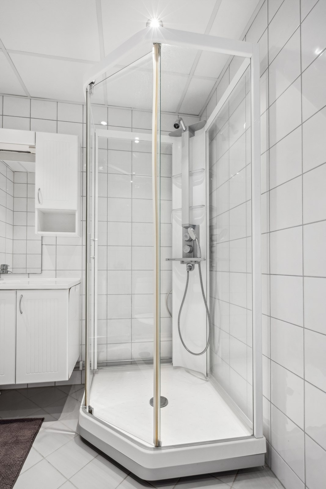 Badet er flislagt og inneholder dusjkabinett, servant, wc og opplegg til vaskemaskin Galleribilde