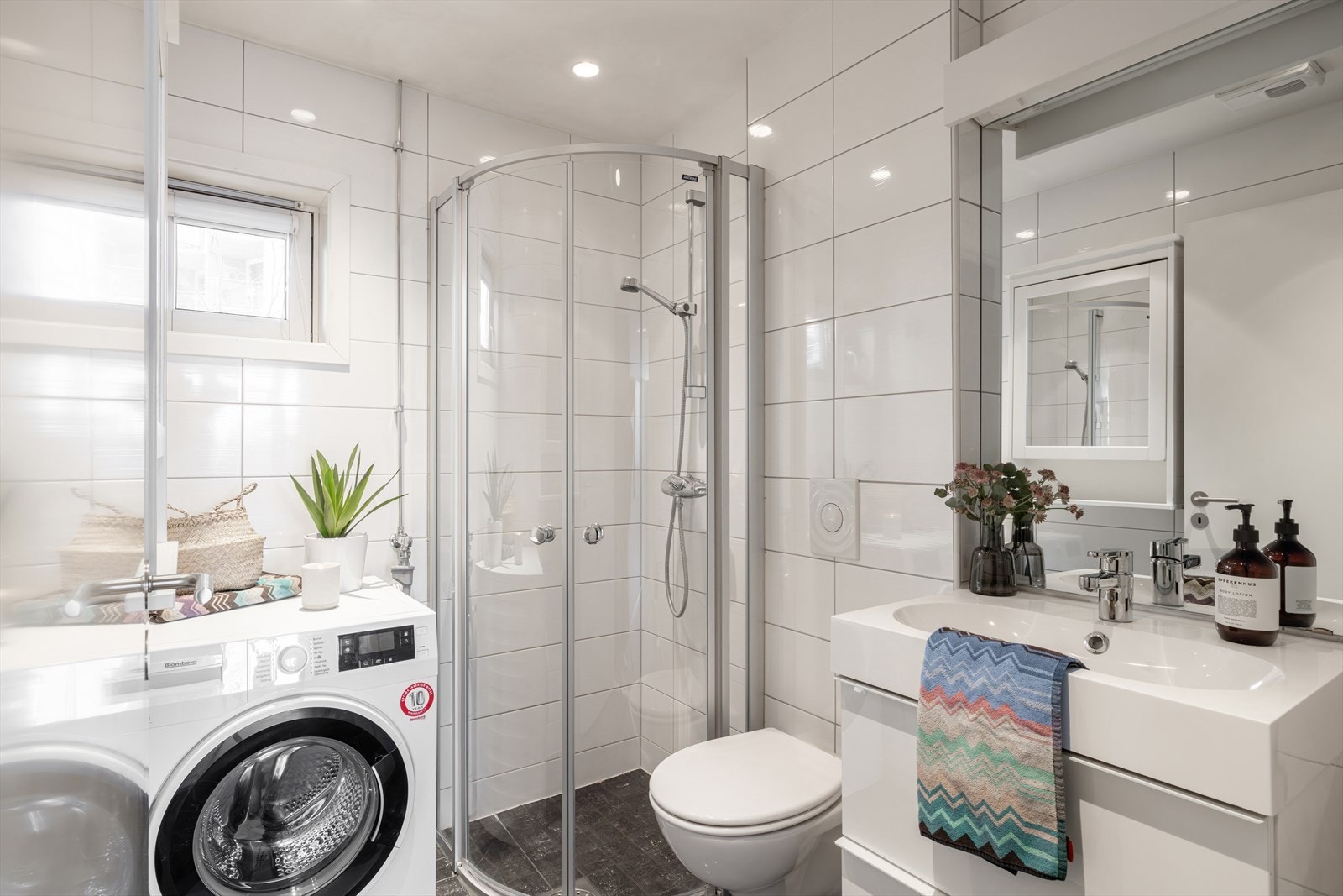 Badet er utstyrt med gulvvarme for ekstra komfort, en heldekkende servant med underskap, speil med belysning, samt et vegghengt klosett. Vindu gir både naturlig lys i rommet samt ytterligere luftemuligheter. Galleribilde