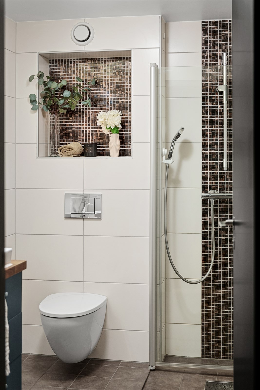 Badet er innredet med vegghengt toalett, baderomsinnredning med speilskap og dusjhjørne med innfellbare glassdører Galleribilde