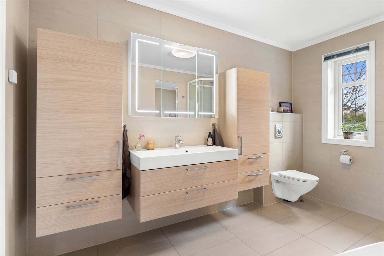 Boligen har to pene bad og et separat vaskerom. Det er ett bad i hver etasje, og begge har sandfargede fliser på vegg- og gulvflater, vannbåren gulvvarme og vegghengte toalett. Galleribilde