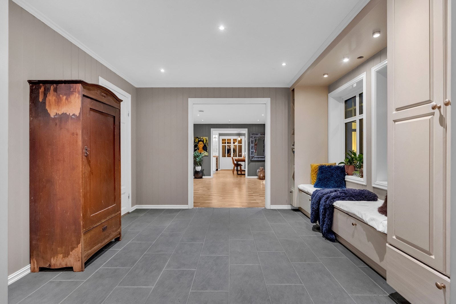 Langs den ene veggen er det to vinduer med dagslys, og rundt vinduene er det en smart, plassbygd garderobeløsning med høyskap, sittebenk med skuffer og belysning. Galleribilde