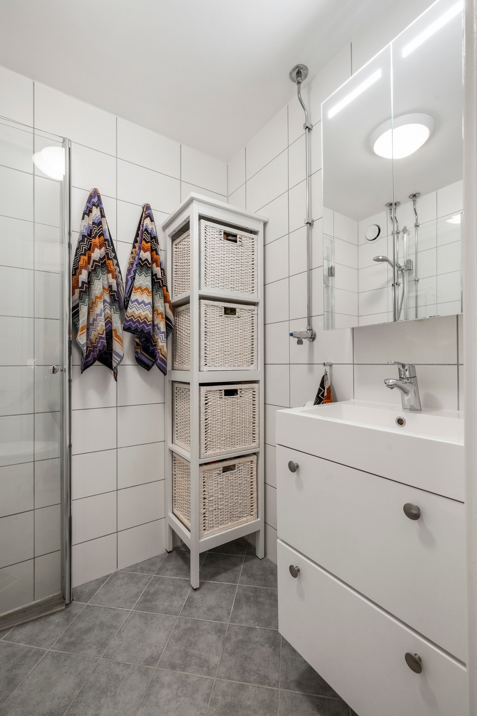 Badet er innredet med servantskap med glatte, folierte fronter og heldekkende servant, speilskap med lysarmatur på vegg over servant og toalett, samt dusjhjørne Galleribilde