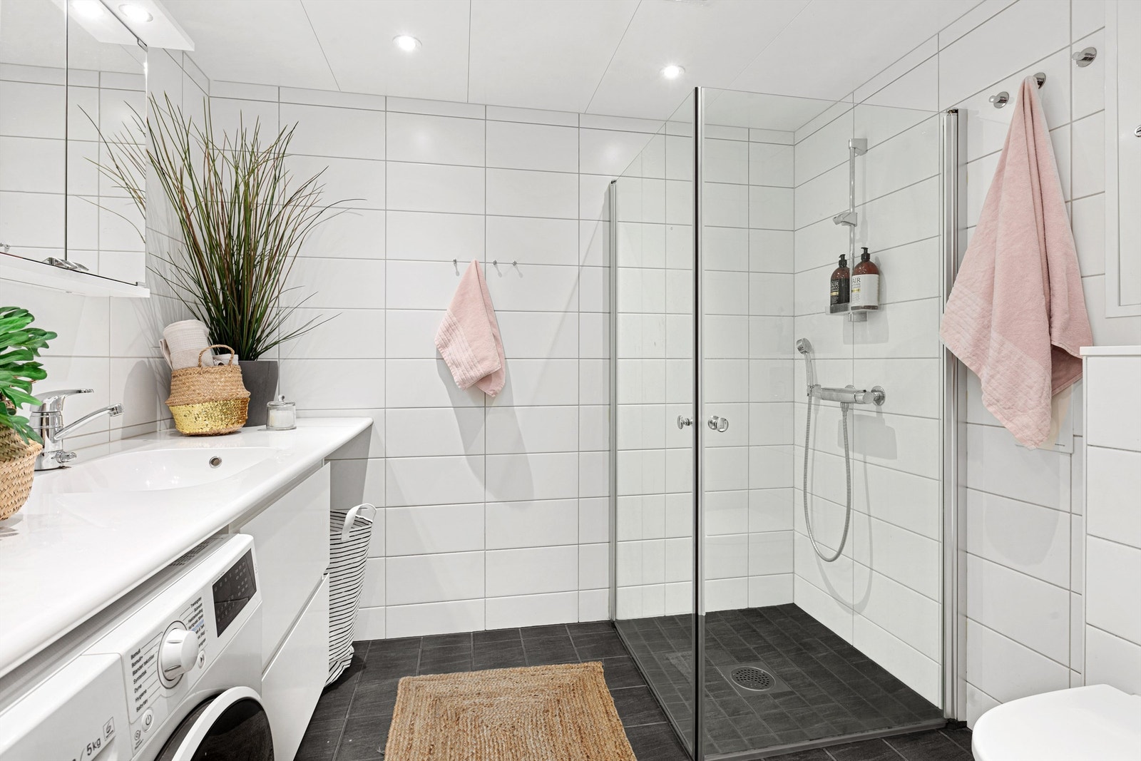 Dusjbad/wc har servantskap med store skuffer, opplegg for vaskemaskin og tørketrommel, og vegghengt toalett. Galleribilde