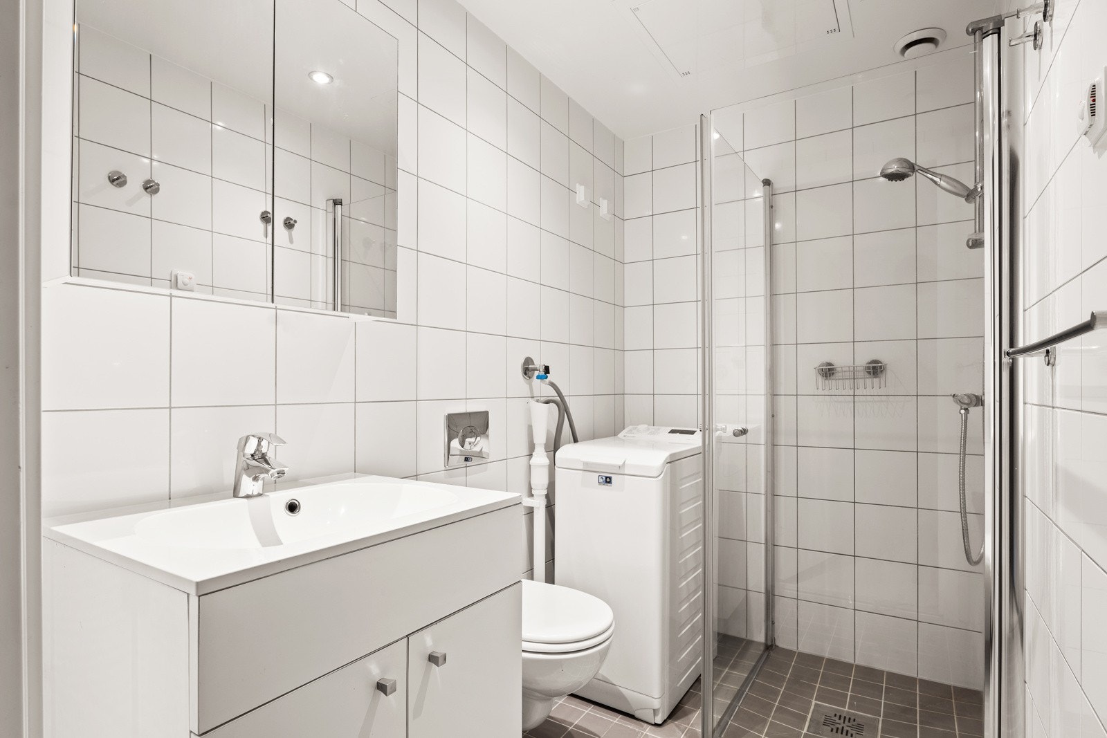 Pent, flislagt bad bestående av dusjhjørne med inn- utadslående dusjvegger, servant m/underskap, overskap m/speilfronter og vegghengt klosett. Galleribilde