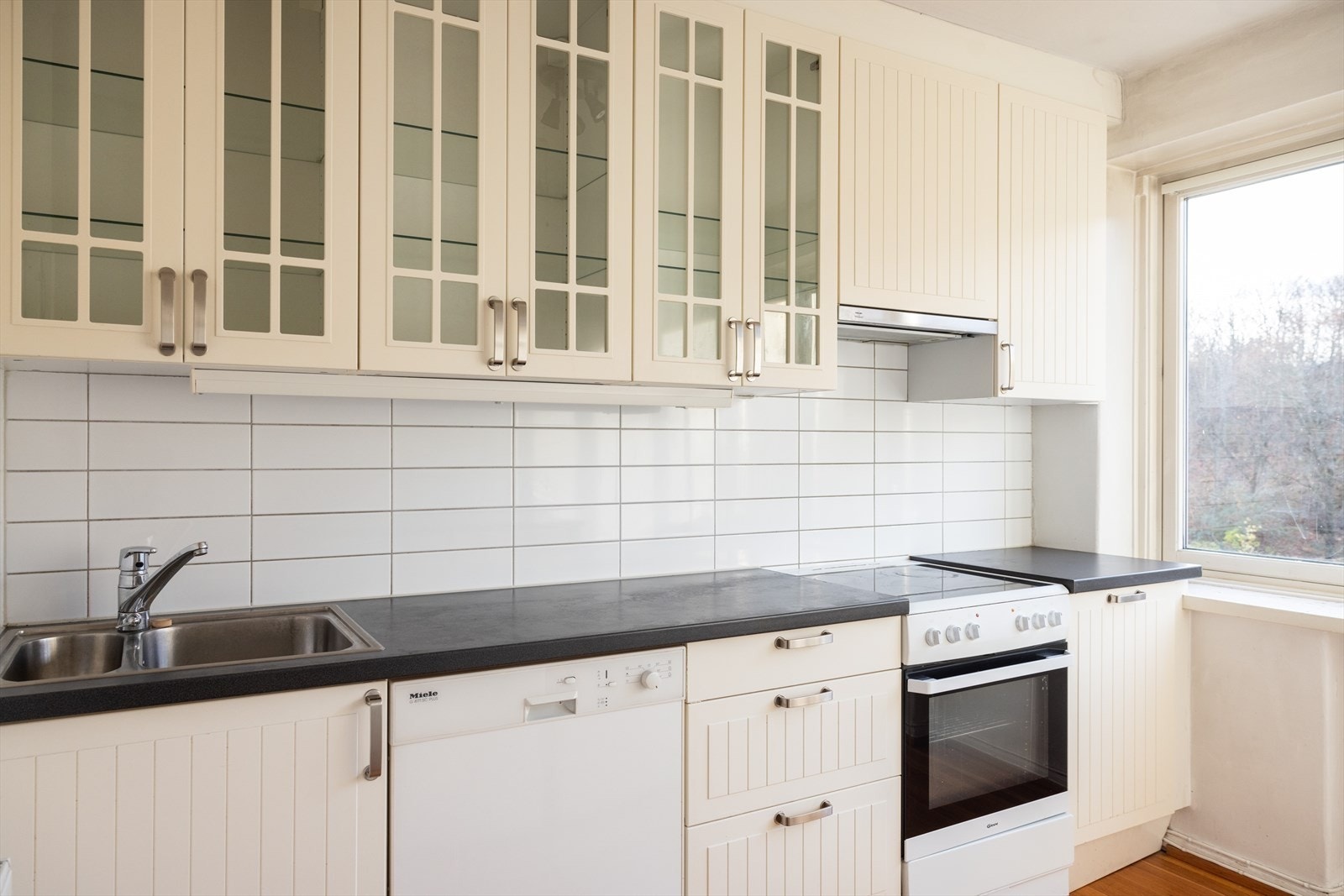 - Kjøkkeninnredning med profilerte fronter. Laminat benkeplate med nedfelt vask-og skyllekum. Fliser over benkeplaten. Avtrekk over kokeplass - Galleribilde