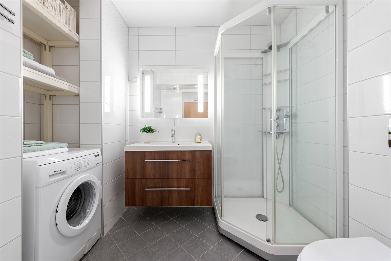 Lyst og tiltalende bad med dusjkabinett og vaskenisje. Praktisk innredning med god oppbevaringsplass og stilren design. Galleribilde