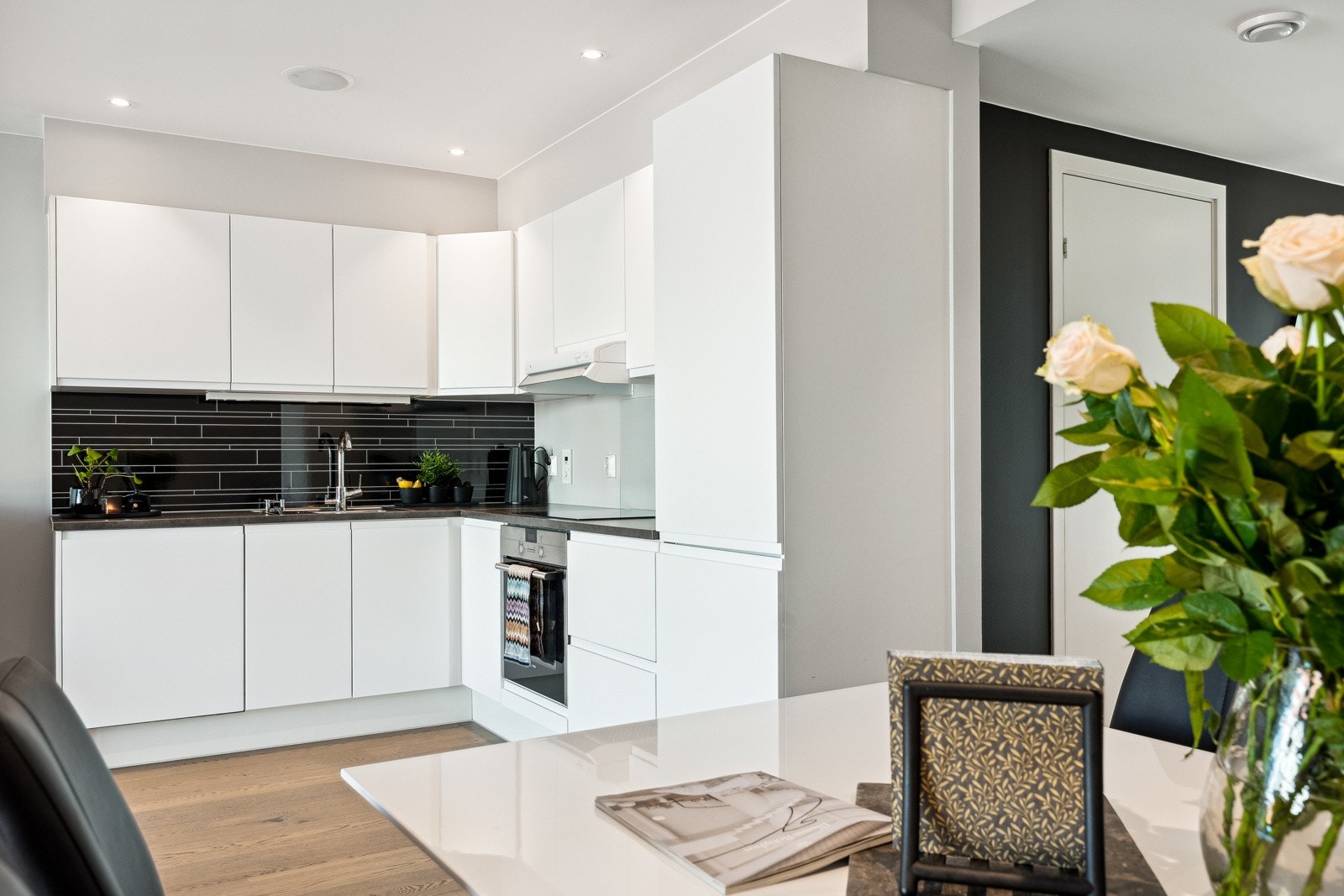 Kjøkkenet har hvite, glatte fronter og integrerte hvitevarer som platetopp, stekeovn, oppvaskmaskin og kombiskap. Galleribilde