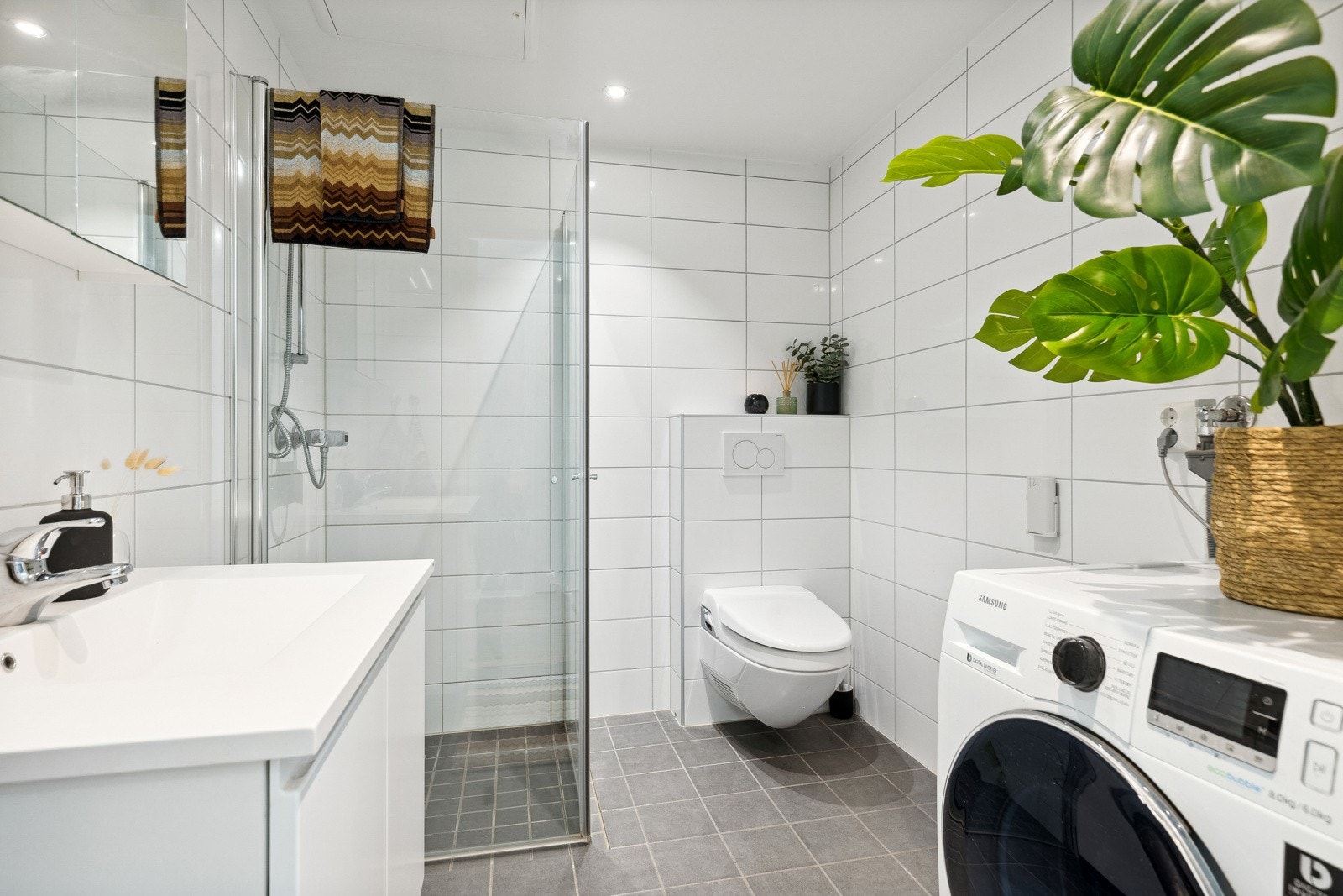 Badet er stilfullt innredet med downlights, hvite veggfliser og mørkegrå gulvfliser med gulvvarme. Galleribilde