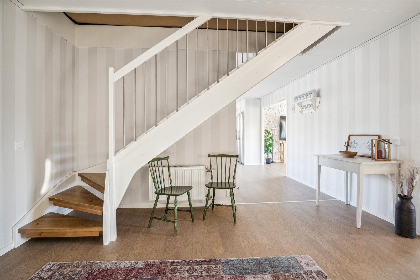 Her kommer du inn i en lys gang med laminat på gulvet og stripete tapet på veggene. Gangen er romslig med trapp opp til 2. etasje etablert i hjørnet av rommet rett innenfor døra. Galleribilde