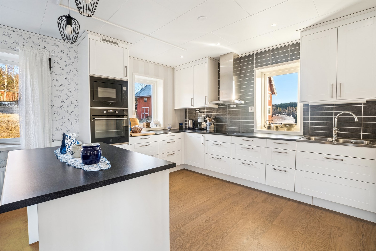 Lys kjøkkeninnredning i hjørneløsning med kjøkkenøy. Innredningen har profilerte fronter, laminerte benkeplater og består av overskap, underskap og skuffer. Galleribilde