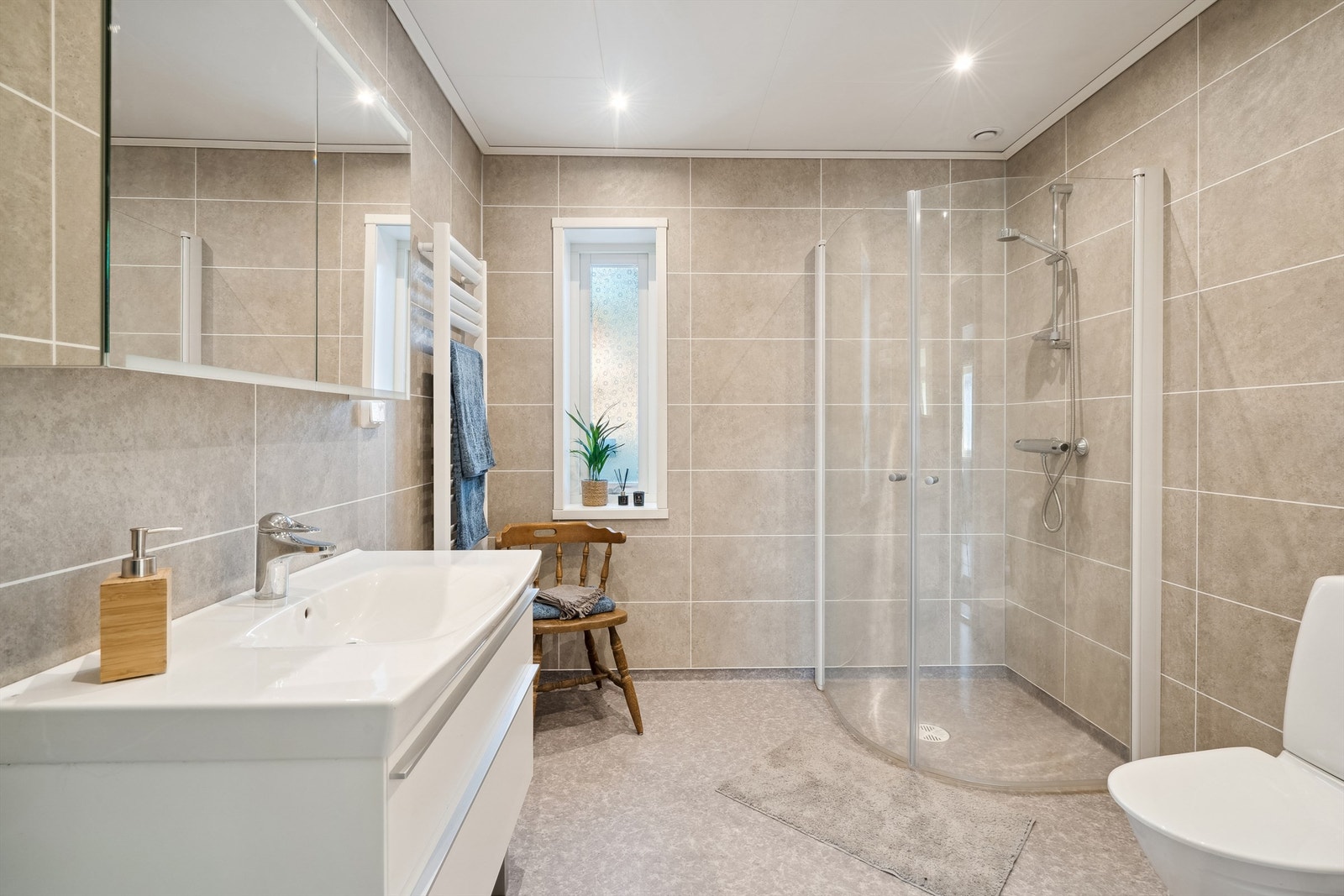 Baderommet har rutete baderomsplater på veggene og lyst belegg på gulvet. Det er elektriske varmekabler som varmekilde i rommet. Galleribilde