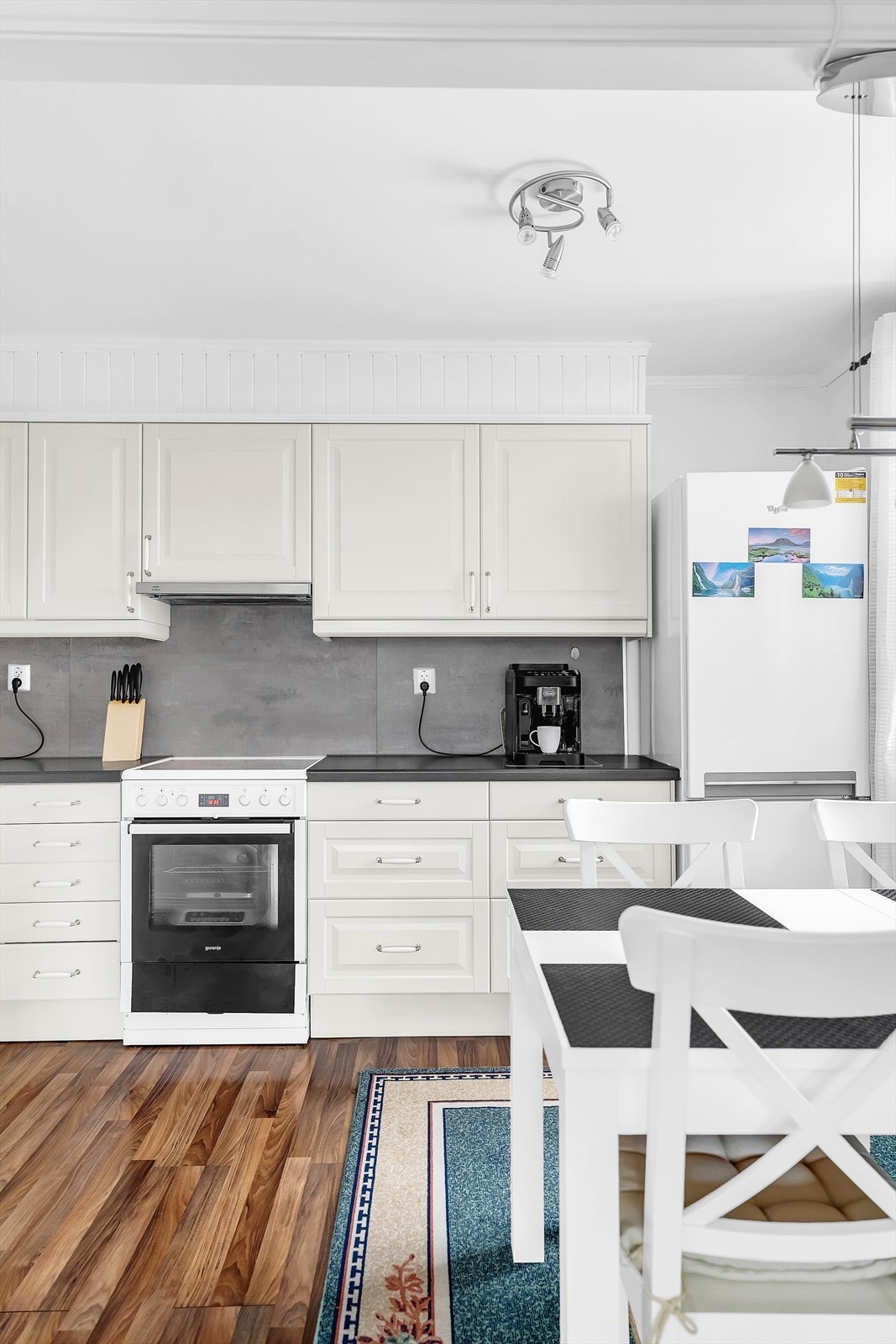 Kjøkkenet har innredning med hvite, profilerte fronter, sort benkeplate i laminat og kitchenboard i gråtoner. Galleribilde