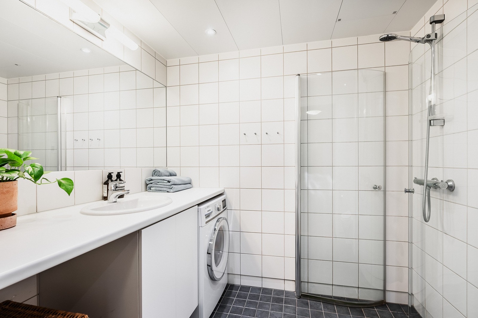 Badet er helfliset og har gulvvarme, downlights, samt nisjer til vaskemaskin og tørketrommel under servantbenk Galleribilde