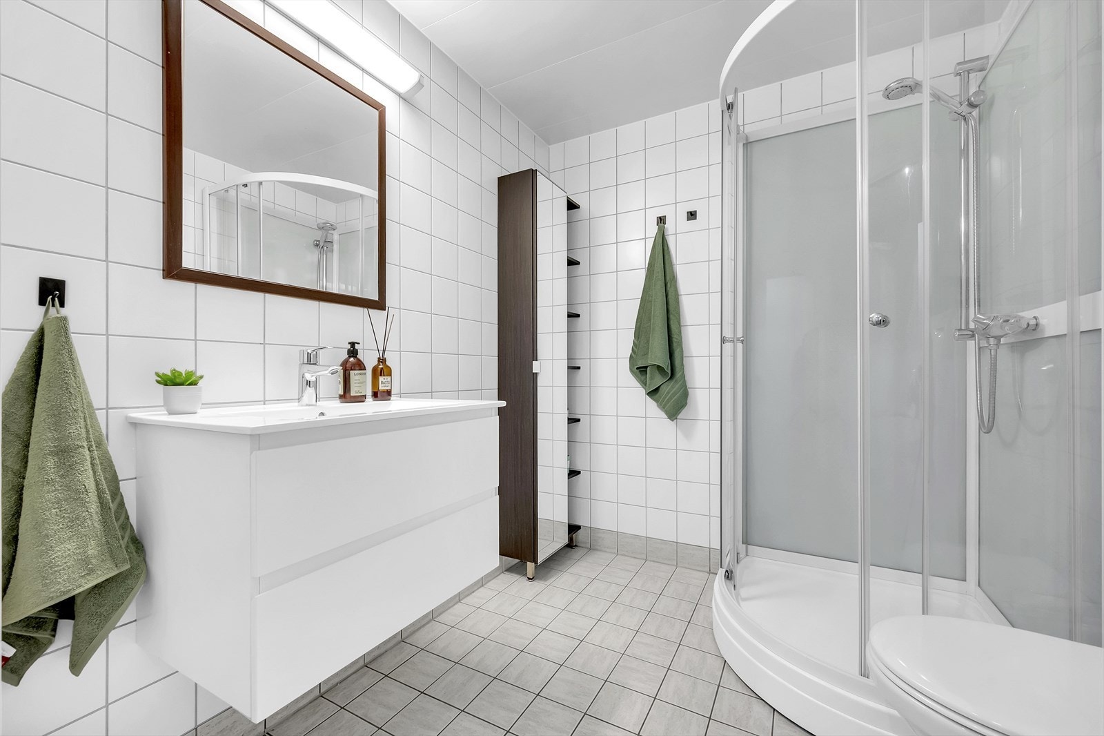 Pent flislagt baderom med varmekabler i gulv, dusjkabinett, toalett og servant med oppbevaring. Galleribilde
