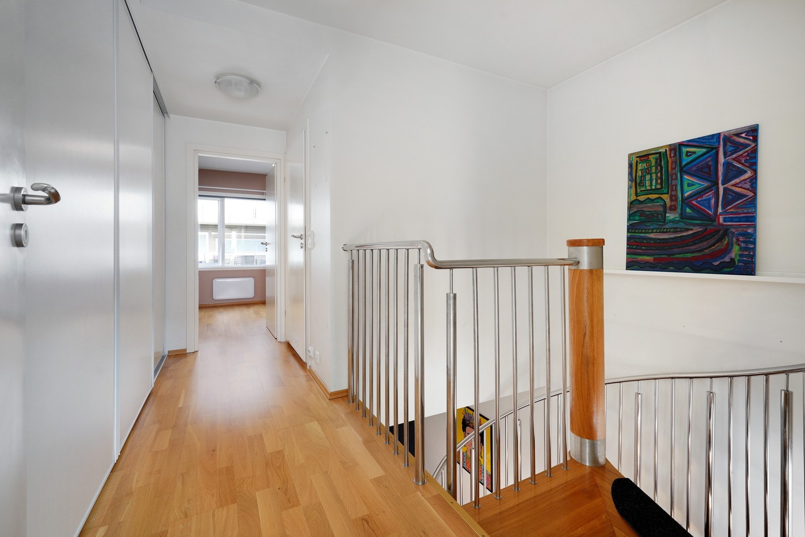 En stilfull vindeltrapp leder til en lys gang med en stor skyvedørsgarderobe. Galleribilde