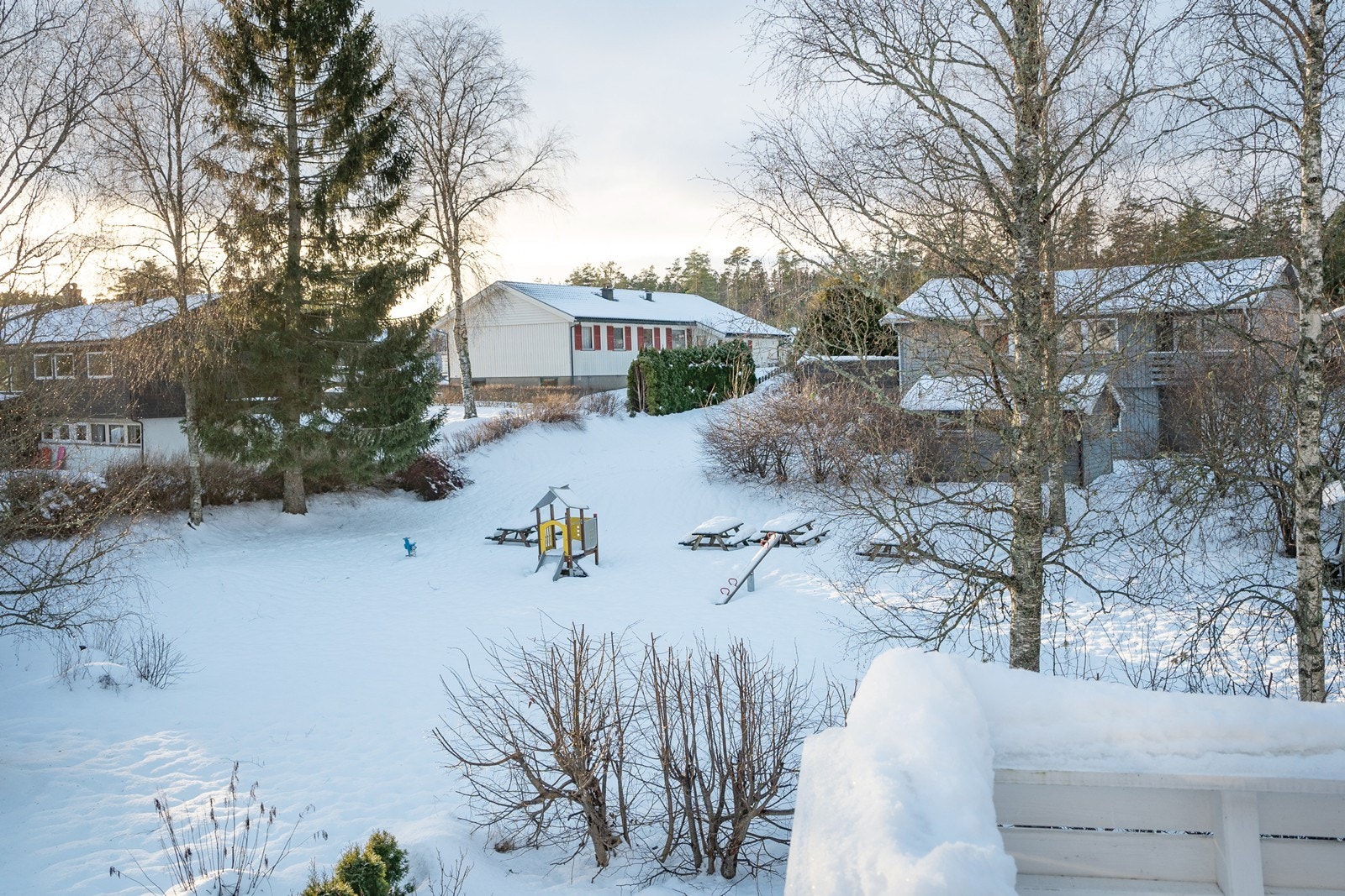 Eiendommen grenser i vest mot et frodig grøntområde med lekeplass og sittebenker. Her med utsikt fra veranda. Galleribilde