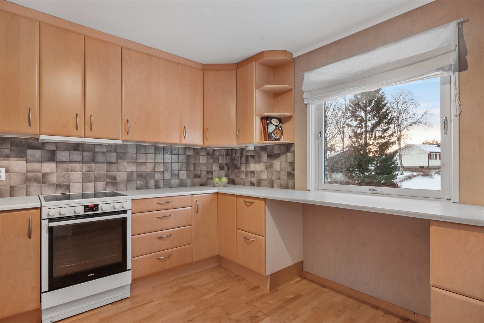 Under et stort vestvendt vindu er en benkeplate med plass til barstoler - et hyggelig frokost- eller kaffehjørne. Galleribilde