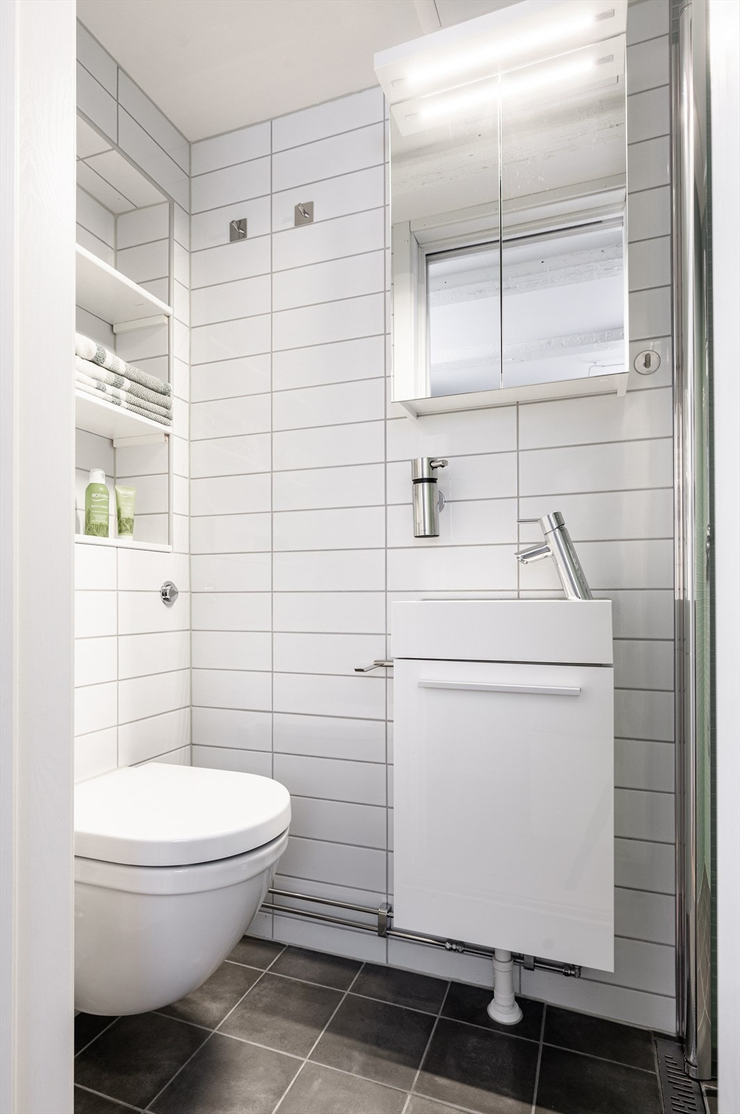 Flislagt bad med dusjnisje, innfellbare dusjdører, vegghengt toalett og servant med ett-greps blandebatteri. Galleribilde