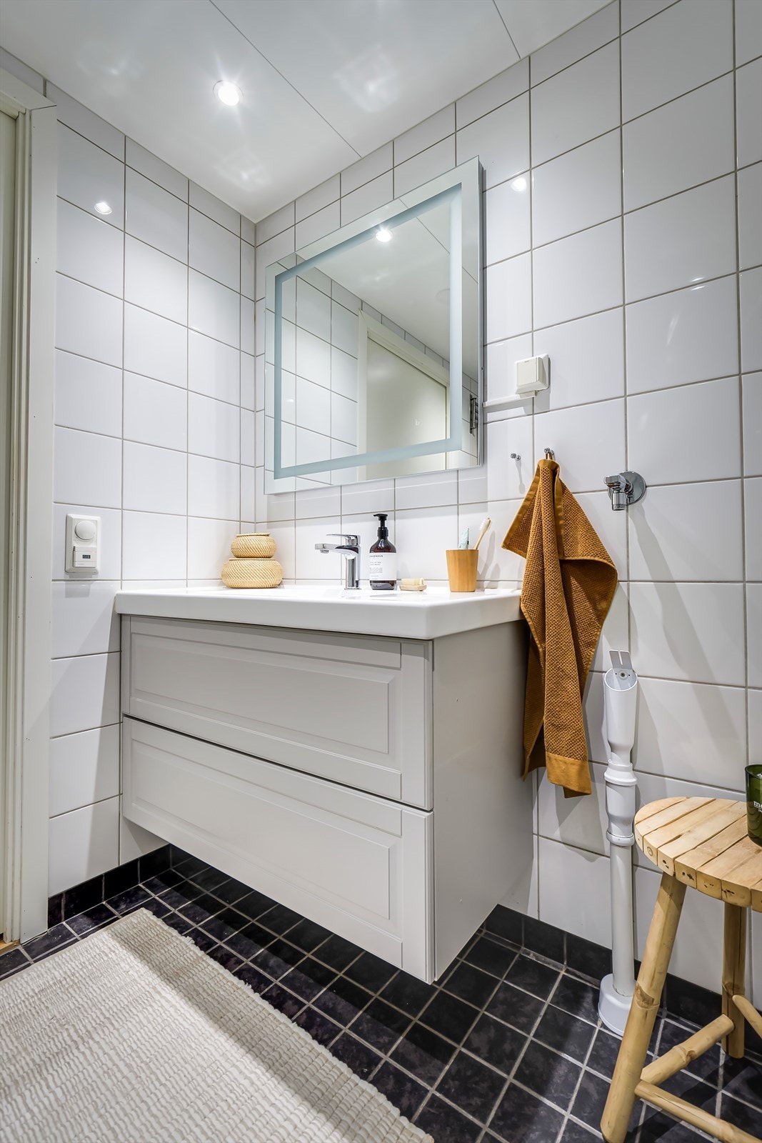 Badet er innredet med servantinnredning med heldekkende servant, speil med sminkelys, veggmontert klosett og dusjhjørne med svingdører i glass Galleribilde